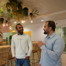 Deux collègues discutent et sourient dans un espace de travail moderne, devant un comptoir lumineux.